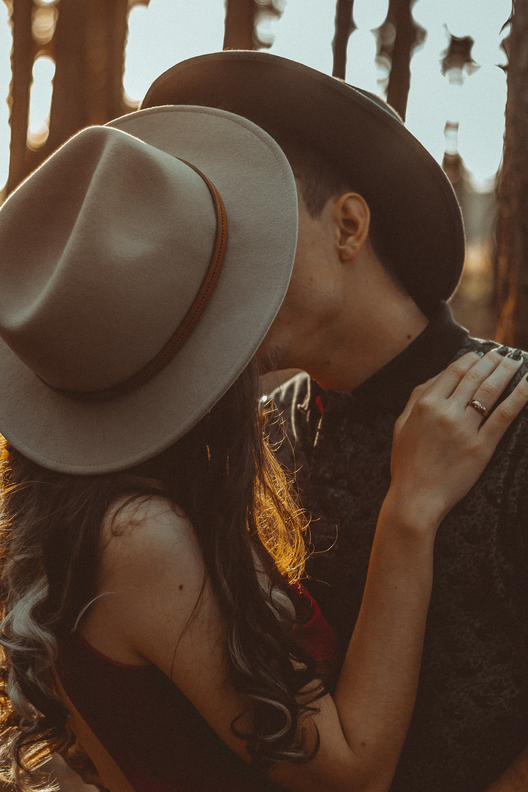 A couple, obscured by wide-brimmed hats, share an intimate moment, highlighting close-up details of their hats and a natural, warm backlight.