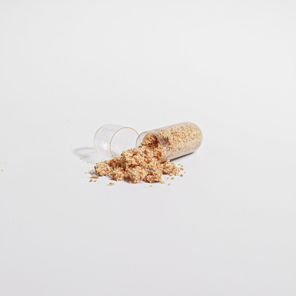 An open capsule with its powdered contents of concentrated Bee Pearl spilled out on a plain white background.