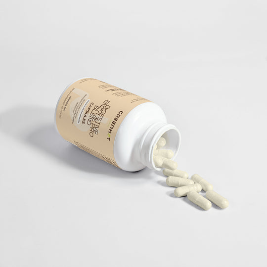 A bottle labeled "GreenHat Digestive Enzyme Pro Blend" tipped over with capsules spilling out on a plain white background.