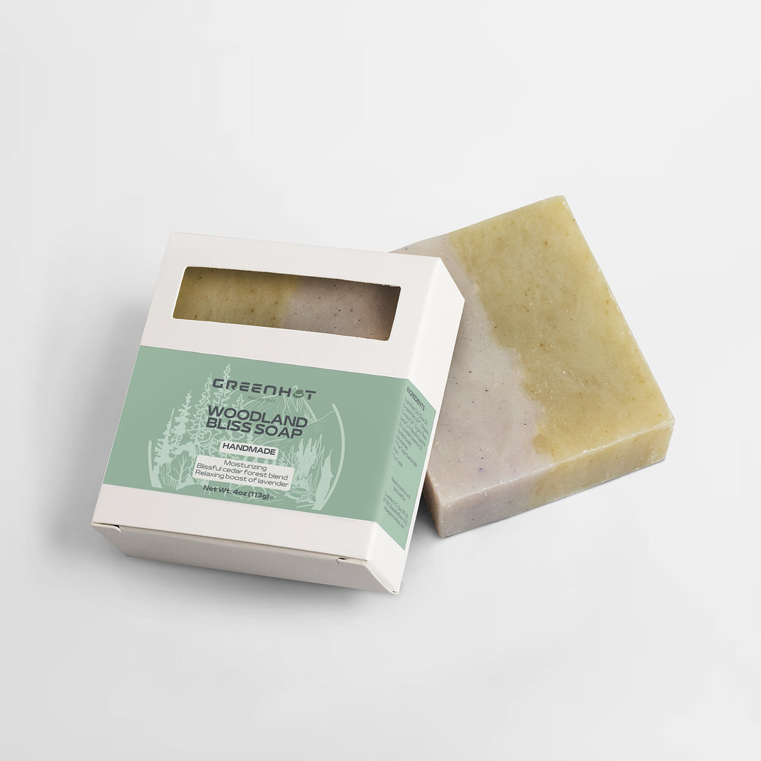 A bar of GreenHat's Woodland Bliss Soap next to its open packaging on a plain white background.