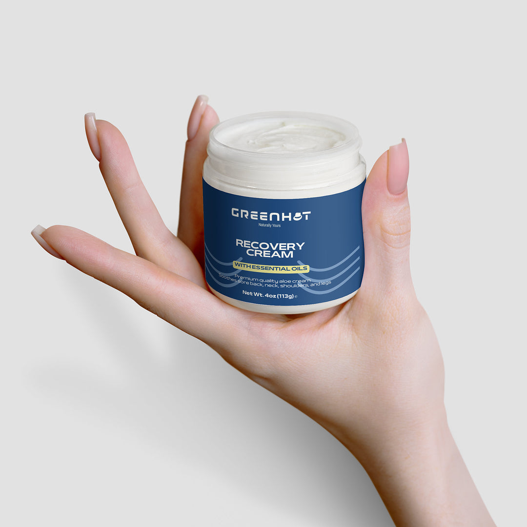 A hand holding a jar of GreenHat premium cosmetic recovery cream against a white background.
