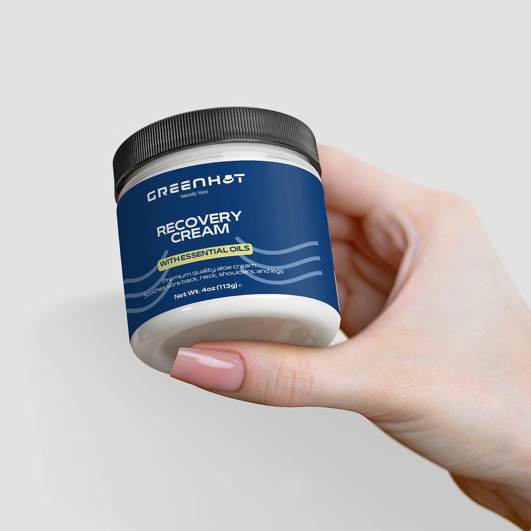 Hand holding a jar of GreenHat premium recovery cream with essential oils, against a white background.