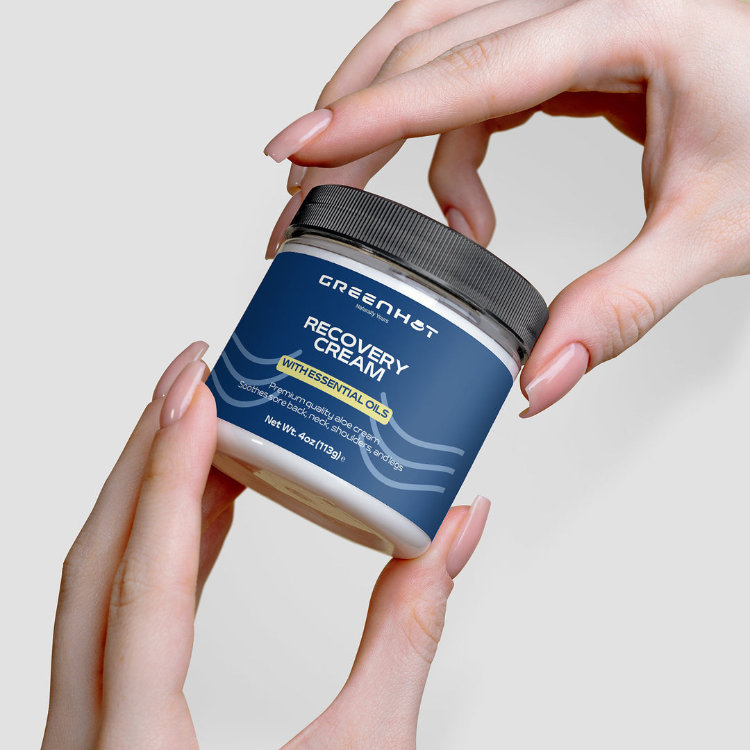 Hands holding a jar of GreenHat premium recovery cream against a plain background.
