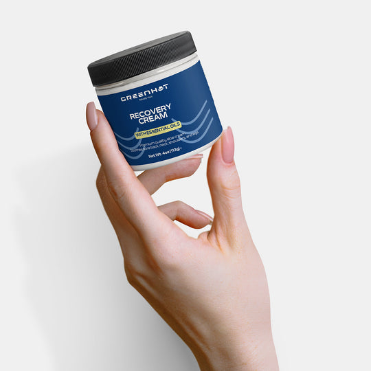 Hand holding a container of premium GreenHat Recovery Cream against a white background.