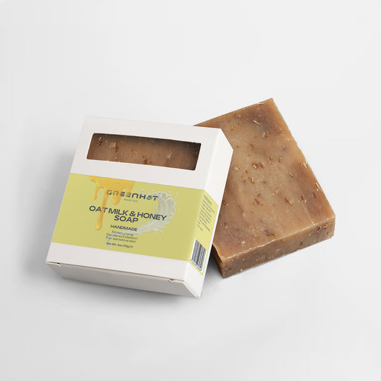 A bar of GreenHat Handmade Oat Milk Honey Soap designed for sensitive skin next to its open packaging on a white background.
