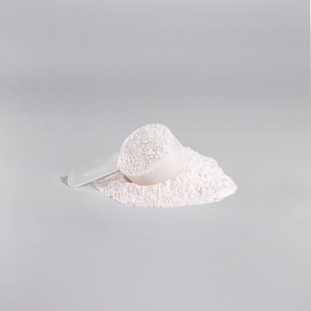 A scoop filled with GreenHat's Nitric Shock Pre-Workout Powder (Fruit Punch) on top of a mound of the same powder, against a light gray background.