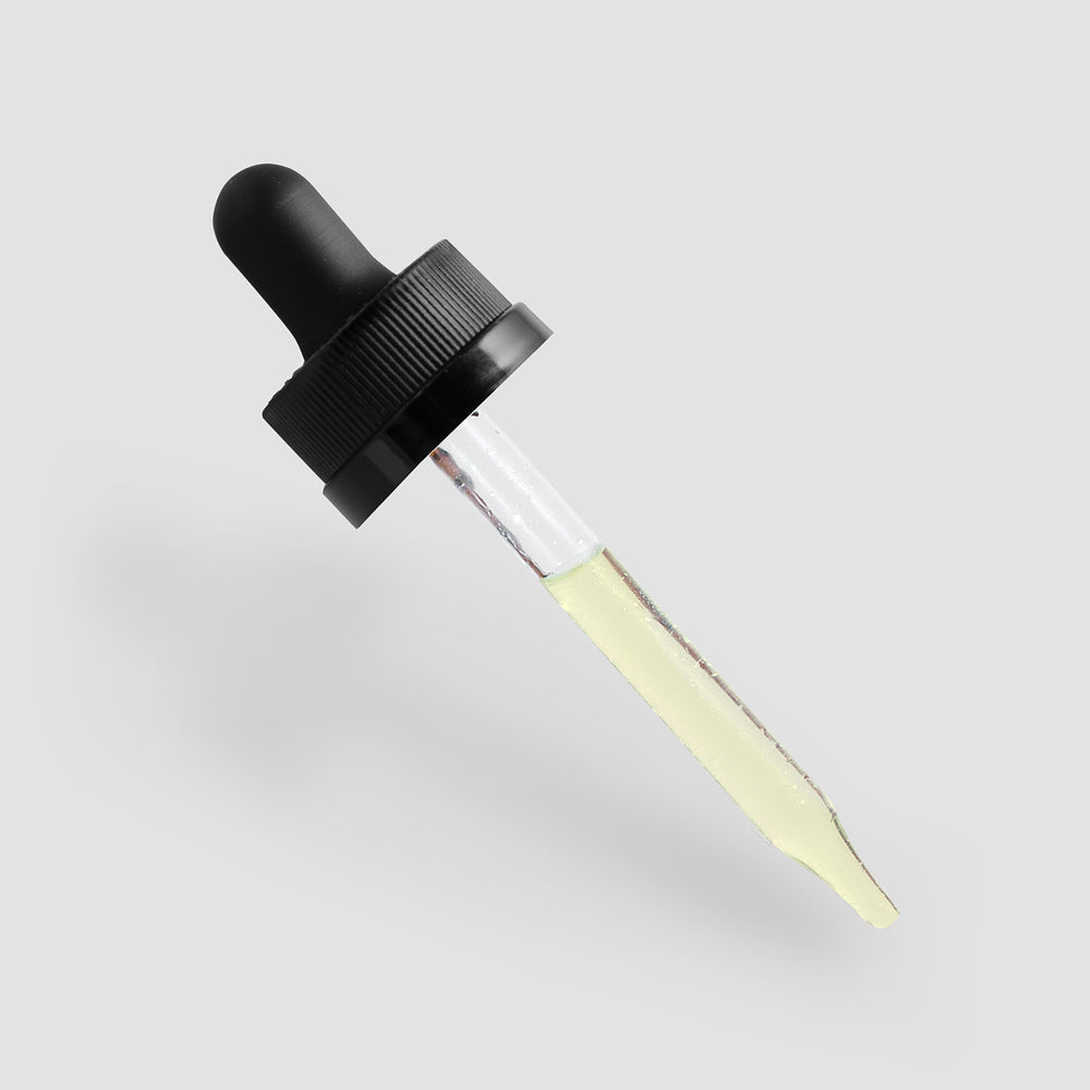 Glass dropper with a black top partially filled with GreenHat's Moisturizing and Strengthening Hair Oil against a light gray background.