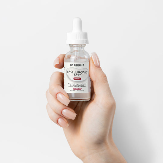 A hand holding a dropper bottle of GreenHat Hyaluronic Acid Serum for multi-layer hydration against a white background.
