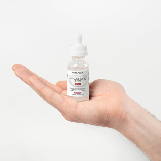 A hand holding a bottle of GreenHat Hyaluronic Acid Serum against a white background.