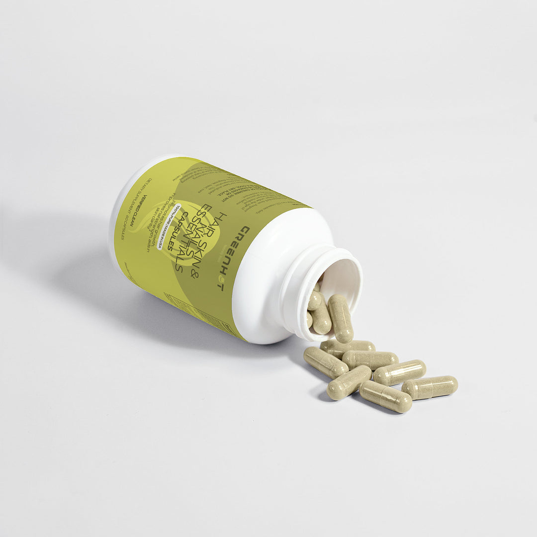 A bottle of GreenHat Hair, Skin and Nails Essentials supplements tipped over with capsules spilling out on a white surface, marketed as a natural beauty elixir for radiant skin.